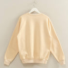 Beige sweatshirt on a hanger against a plain wall