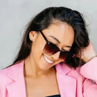 Woman wearing sunglasses and a pink blazer against a gray background