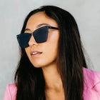 Woman wearing dark sunglasses and a pink blazer against a gray background
