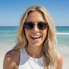 Woman wearing sunglasses on a beach with clear blue water and sky.