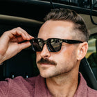 Man wearing sunglasses sitting inside a vehicle with a blurred outdoor background