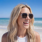 Woman wearing sunglasses on a beach with clear blue sky and ocean.