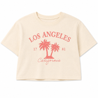 A cream-colored short-sleeve crop top t-shirt featuring a coral-pink graphic print of two palm trees, the text 'LOS ANGELES', 'California', and the numbers '17' and '81' on the front, displayed against a solid white background.
