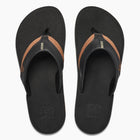 A pair of black Reef flip-flops with a brown leather strap detail, shown from a top-down view on a light gray background.
