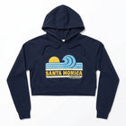 A navy blue cropped pullover hoodie with a retro Santa Monica California graphic on the chest, featuring a yellow sun, blue waves, and yellow text, displayed on a clean white background.