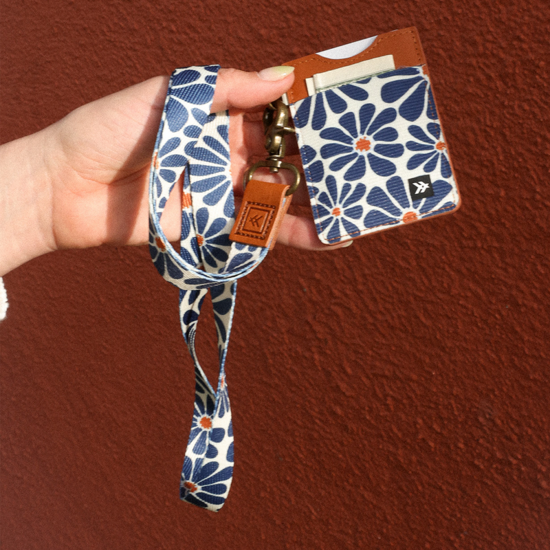 Hand holding a floral-patterned lanyard with a matching cardholder against a brown background
