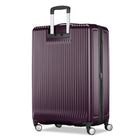 A hard-shell carry-on suitcase in deep plum purple with vertical grooves, featuring an extended silver telescoping handle and four spinner wheels, shown on a plain white background.
