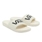 A pair of off-white slide sandals with a bold black Vans logo printed across the straps, set against a light gray studio background.