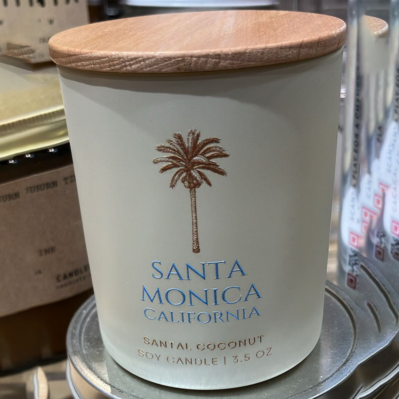 Candle with wooden lid labeled 'Santa Monica, California' on a store shelf.
