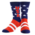 A pair of crew socks with a patriotic USA theme, featuring a navy blue upper half with white stars and red 'USA' lettering, a red and white striped lower half, and navy blue toes and heels. The brand name 'COOL' is printed near the toes.