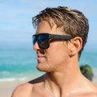 Man wearing sunglasses on a beach with ocean and sky in the background