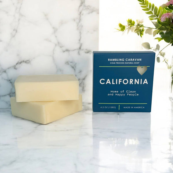 Bar of soap and blue packaging on a marble surface with flowers in the background