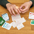 Person applying a bandage to a finger with an open first aid kit on a wooden surface.