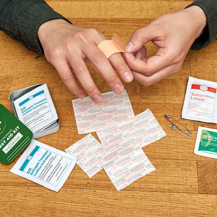 Person applying a bandage to a finger with an open first aid kit on a wooden surface.