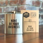 Stainless steel flask with 'None of Your Business' text and packaging on a wooden surface.
