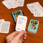 90s Music trivia game cards on a wooden surface with a hand holding a card.