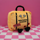 Plush toy suitcase labeled 'Emotional Baggage' on a pink and white checkered floor.