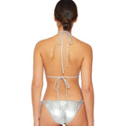 A woman shown from the back wearing a metallic silver string bikini against a plain light gray studio background.