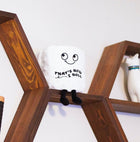 White pillow with black text and black legs on a wooden shelf