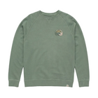 A sage green crewneck sweatshirt with raglan sleeves and a small circular multicolor graphic on the left chest, displayed flat against a light gray background.
