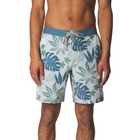 A man wearing board shorts with a tropical leaf pattern in shades of blue, teal, and white, featuring a solid blue waistband with a white drawstring.