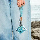 Person holding a blue lanyard with a card holder against a beach background