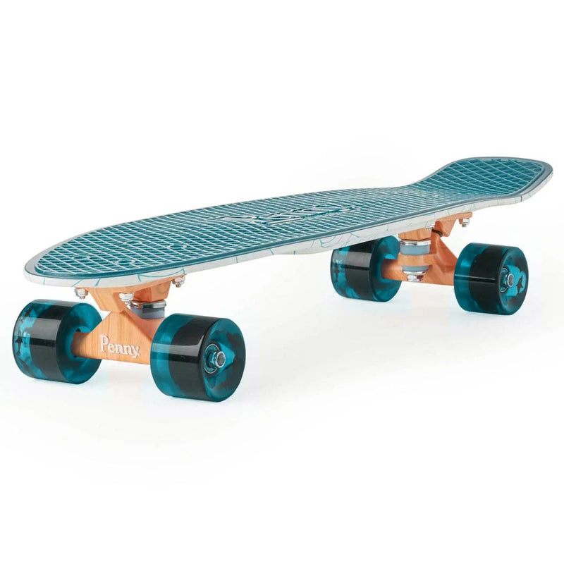 Side angle view of a Penny skateboard showing its teal textured deck, light wood-colored trucks with 'Penny' branding, and teal translucent wheels. The deck has a slight kicktail, and the edges reveal the wave pattern from the undersid