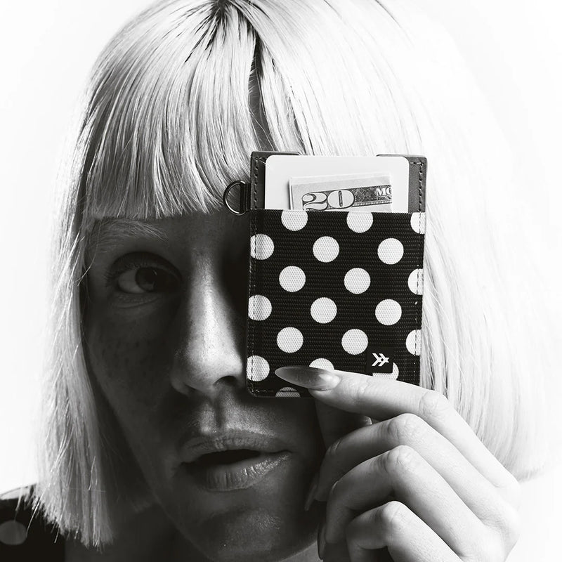 Person holding a black wallet with white polka dots in front of their face