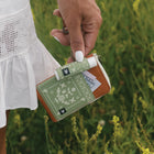 Hand holding a green and brown wallet with a blurred natural background
