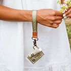 Person holding a keychain with a small bottle and flowers, wearing a white outfit.