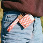 Person wearing a red and white checkered wallet with a strap over their shoulder outdoors.