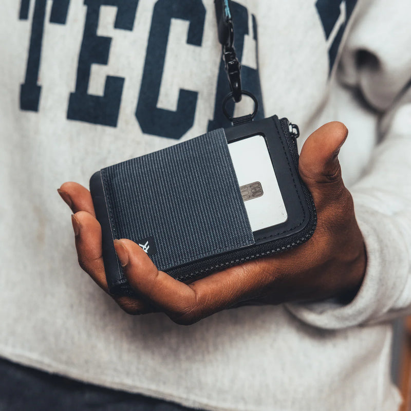 Person holding a black wallet with a visible brand logo against a blurred background